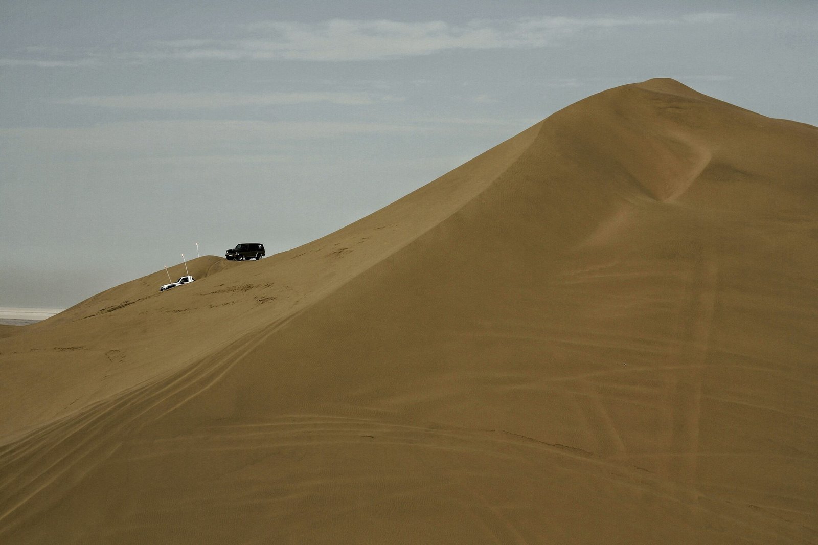 A red 4x4 vehicle climbing a steep sand dune