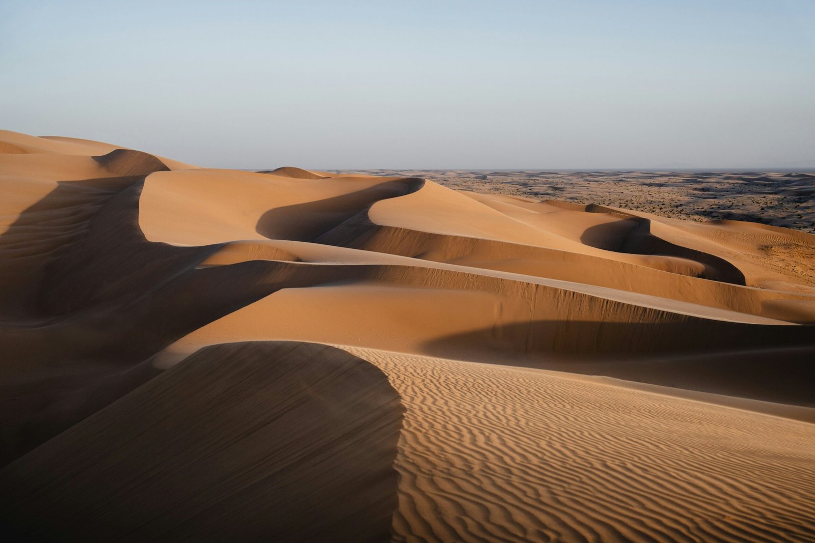 A red 4x4 vehicle driving over large sand dunes during sunset