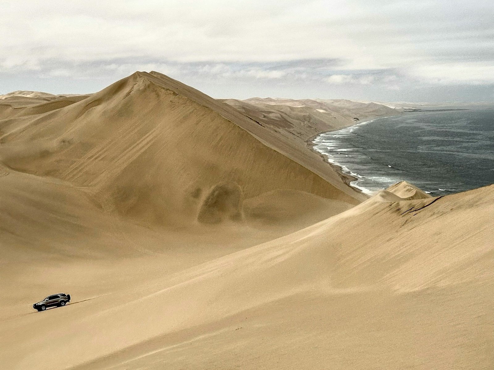 A rugged 4x4 driving up a steep desert dune against a glowing sunset