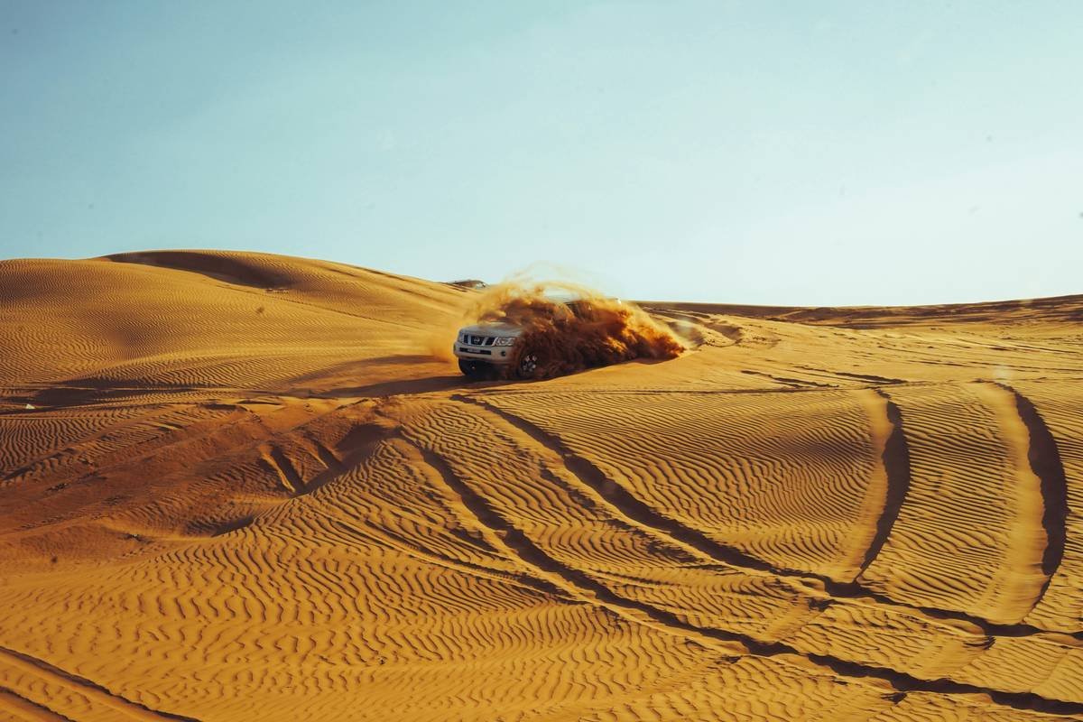 Golden sand dunes under a blue sky with a 4x4 vehicle racing downhill.