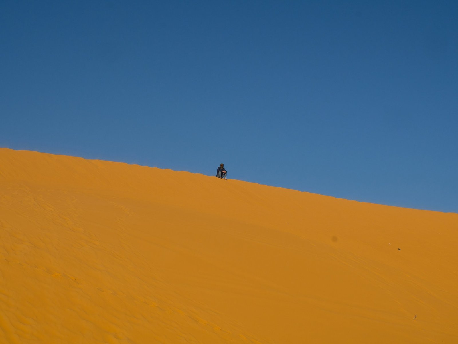 Tourists enjoying sandboarding on steep golden dunes