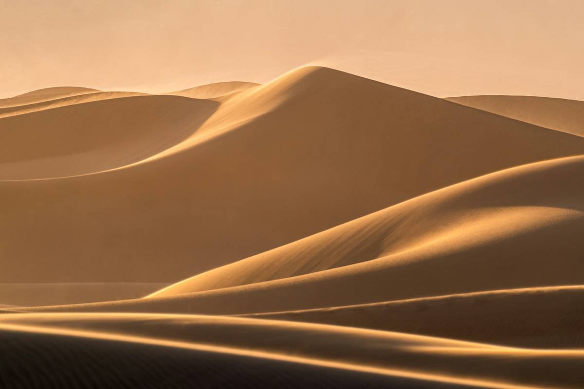 Aerial view of golden desert dunes under blue skies.
