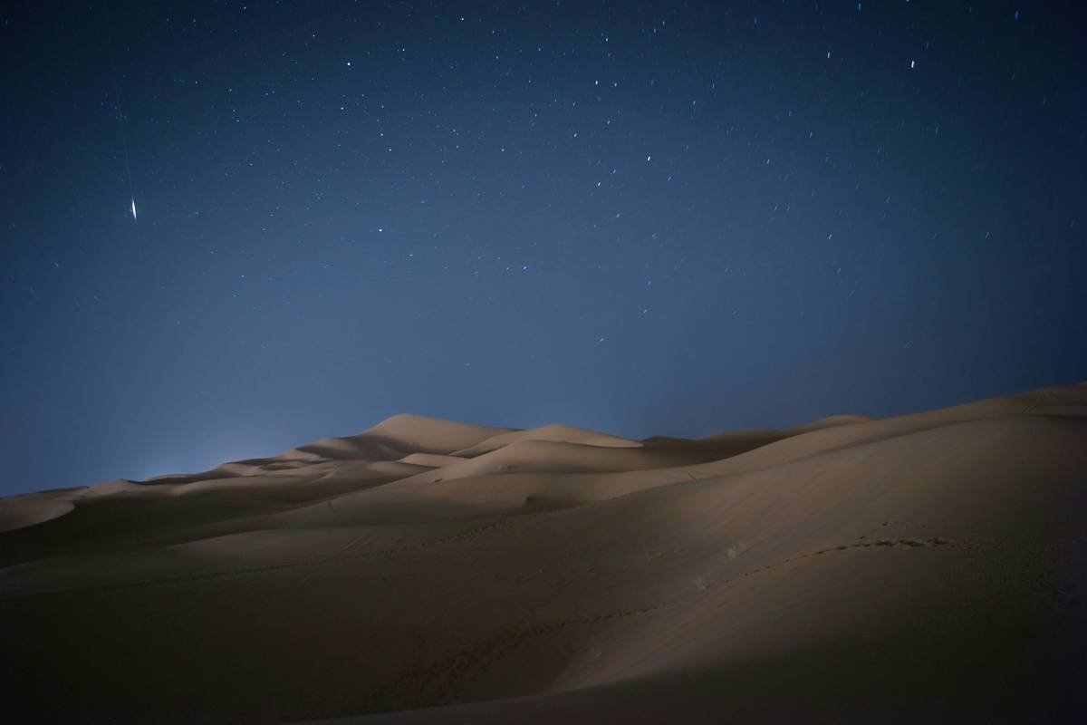 A cozy campsite setup beside dunes, featuring warm fireside lighting and relaxed travelers enjoying the evening ambiance.