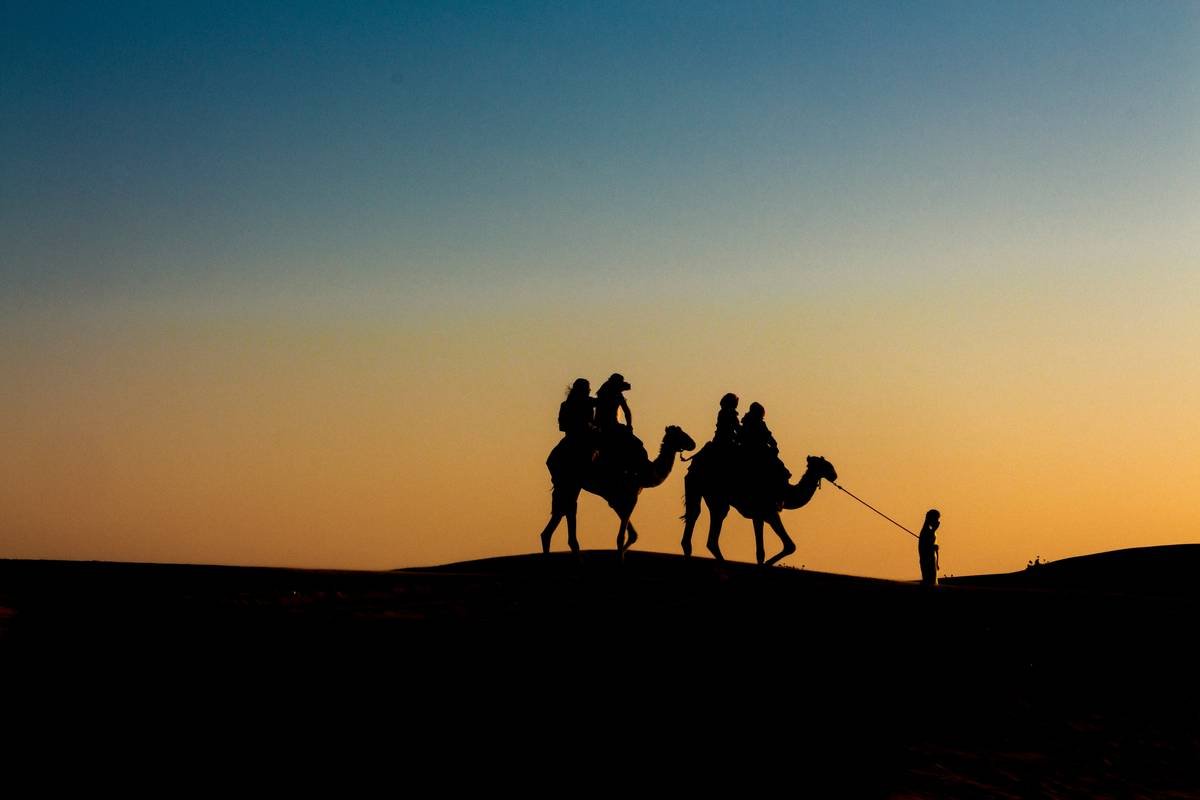 Tourists riding camels through vast desert landscape